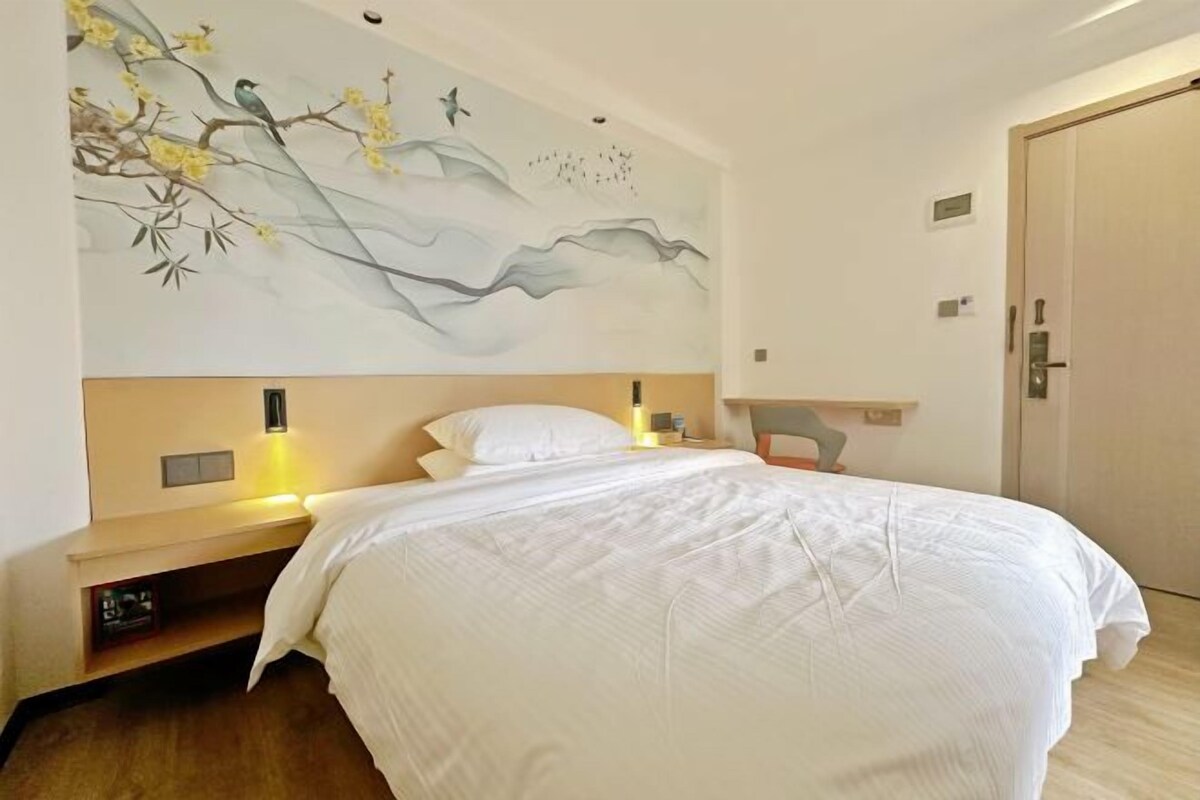 Une chambre d’hôtel avec un lit, une table de chevet, une commode, des œuvres d’art murales et une porte.