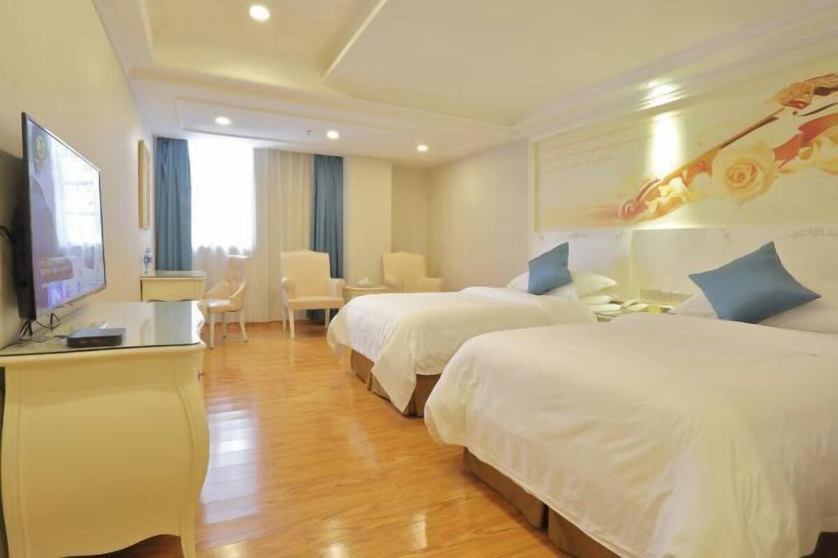 A hotel room with two beds, a desk with a TV, a chair, and a window with curtains.