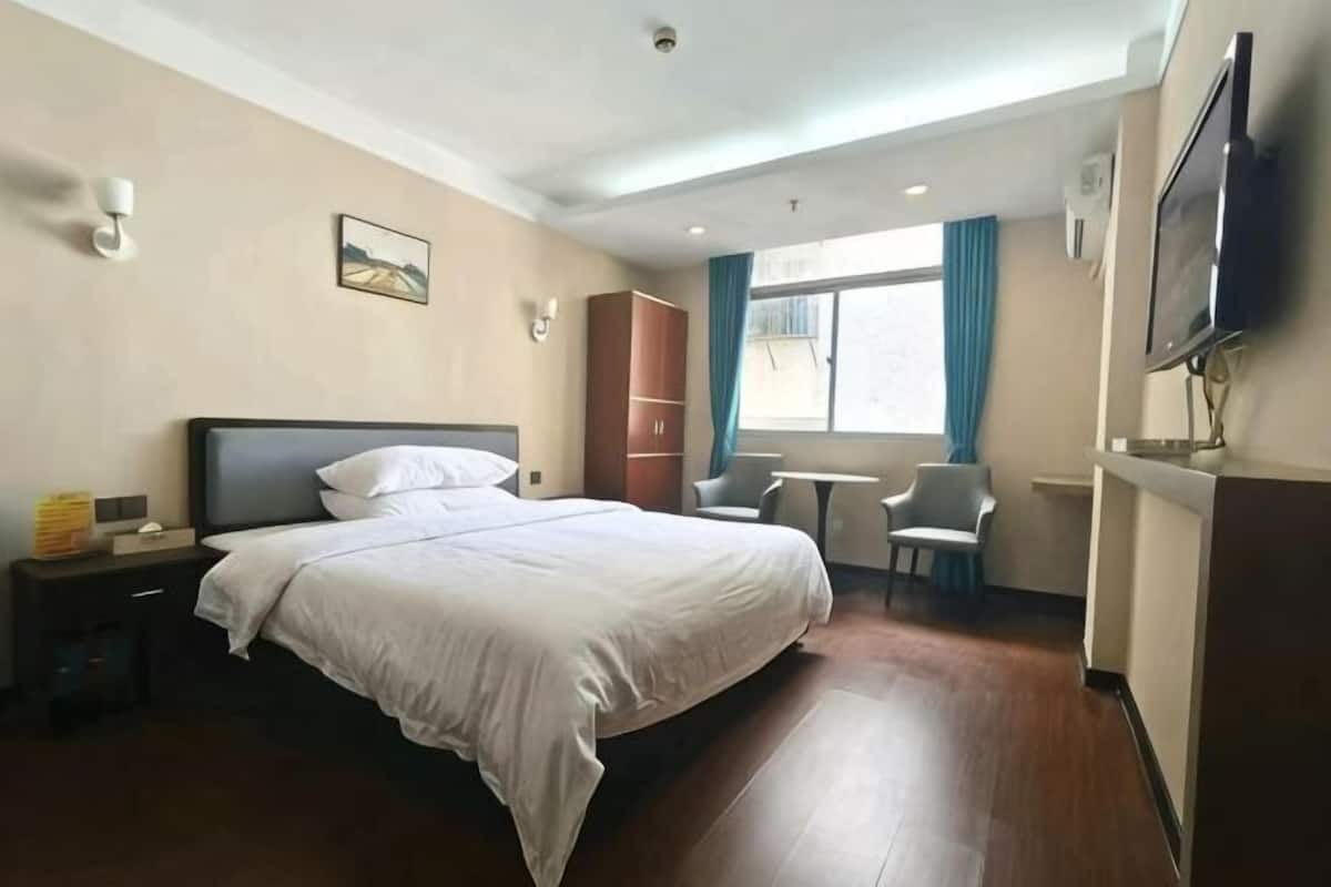 A hotel room with a bed, a desk, a chair, a TV, and a window with curtains.