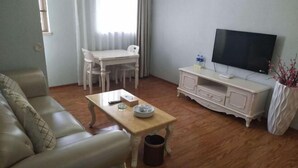 A living room with a sofa, a coffee table, a TV, a dining table with chairs, and a cabinet. - Hongxing Boutique Hotel (Shantou)