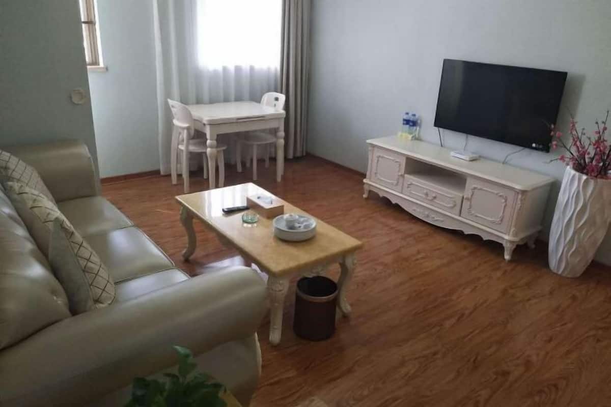 A living room with a sofa, a coffee table, a TV, a dining table with chairs, and a cabinet.