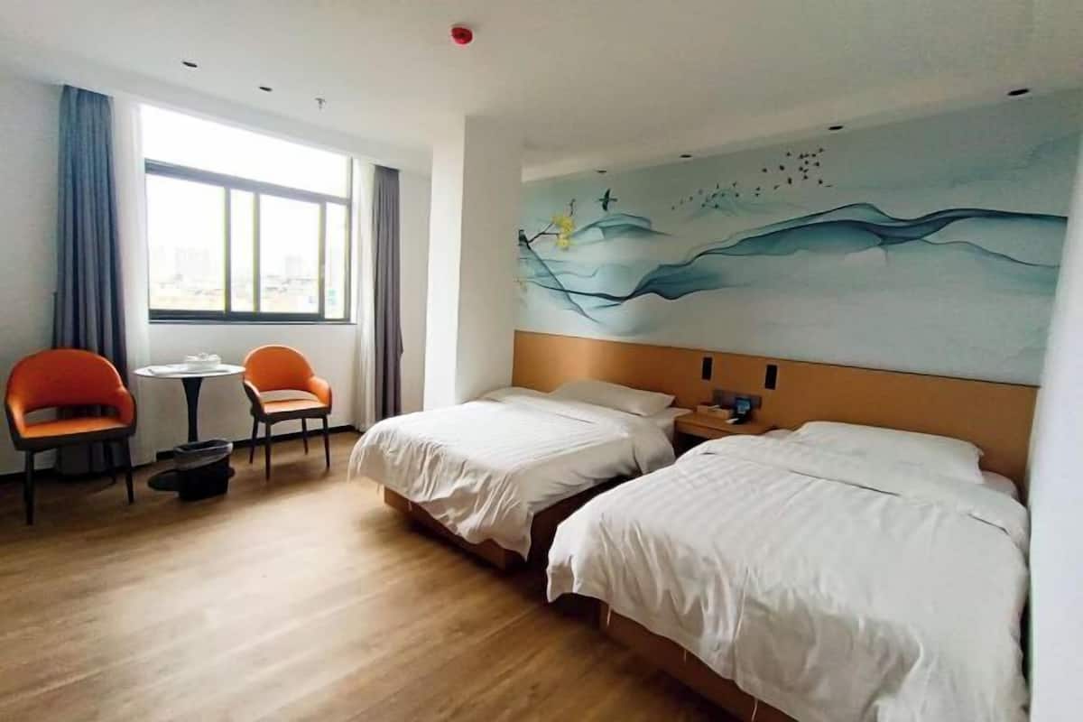 A hotel room with two beds, a small table, two chairs, and a large window with curtains.