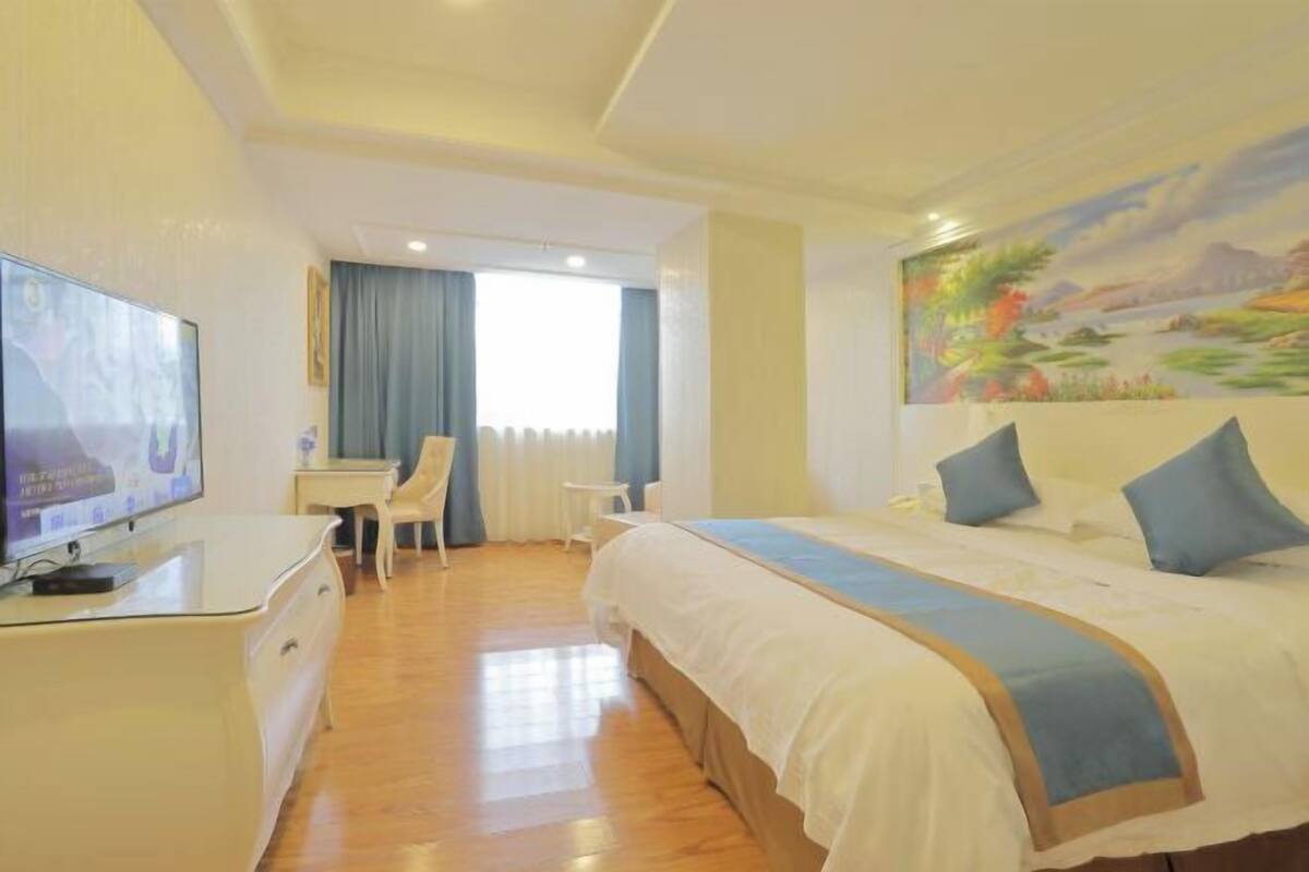 A hotel room with a bed, a desk with a TV, a chair, and a painting on the wall.