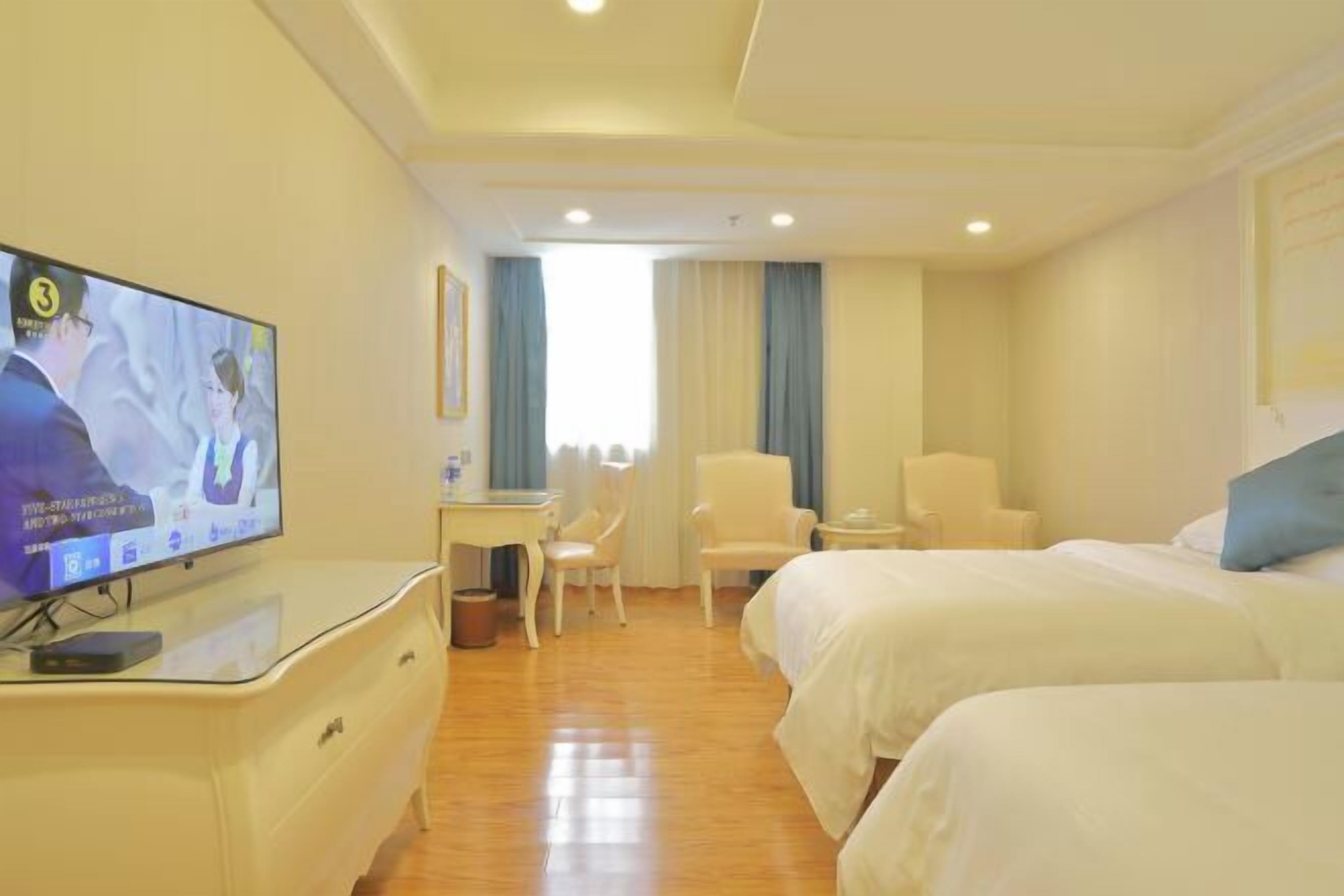 Ein Hotelzimmer mit zwei Betten, einem Schreibtisch, einem Stuhl, einem Fernseher und einem Fenster mit Vorhängen.