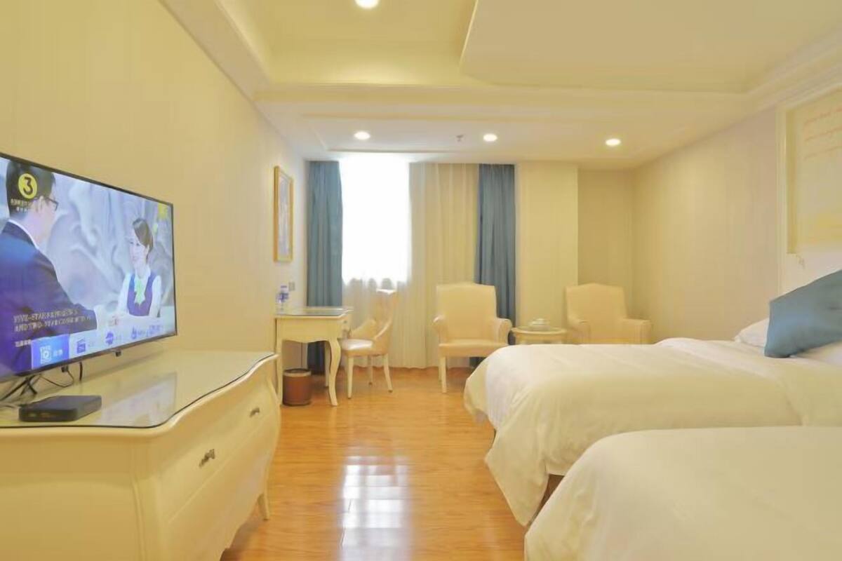 A hotel room with two beds, a desk, a chair, a television, and a window with curtains.