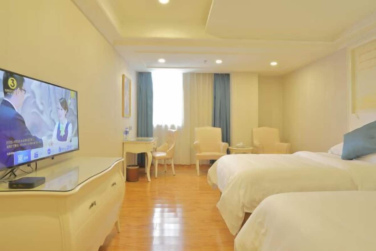 Ein Hotelzimmer mit zwei Betten, einem Schreibtisch, einem Stuhl, einem Fernseher und einem Fenster mit Vorhängen.