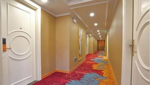 A hotel corridor with a red carpet featuring a leaf pattern, white doors with circular handles, and recessed lighting on the ceiling. - Hongxing Boutique Hotel (Shantou)