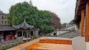 A traditional Chinese pavilion with a tiled roof, surrounded by lush greenery and stone walls. - Aunty Ji Inn (Tongxiang)