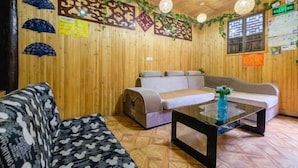 A room with wooden walls, a sofa, a loveseat, and a glass coffee table. - Aunty Ji Inn (Tongxiang)