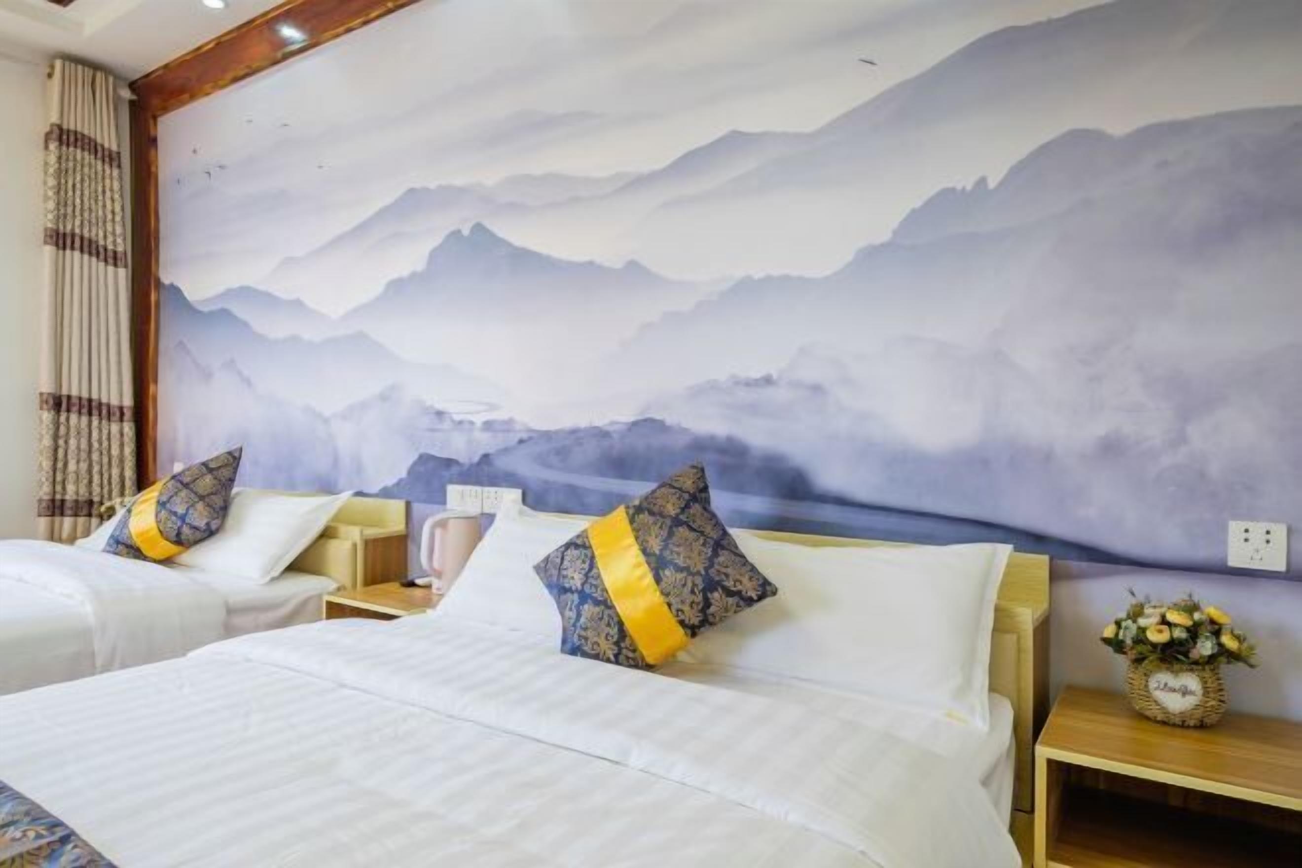 Habitación de hotel con dos camas, un mural grande de montañas y una mesita de noche de madera con un florero.