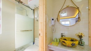 A bathroom with a toilet, a glass shower enclosure, a mirror, and a sink with a yellow bowl. - Aunty Ji Inn (Tongxiang)