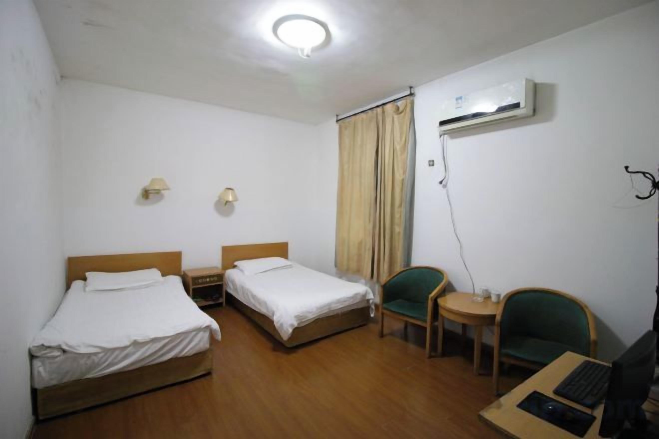 Habitación de hotel con dos camas individuales, un escritorio con silla, una mesita pequeña y un equipo de aire acondicionado.