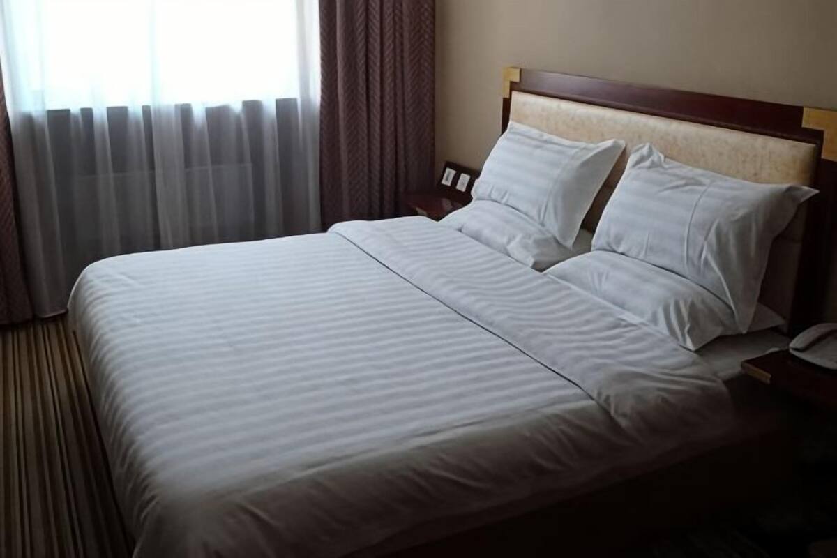 A hotel room with a large bed, a nightstand, and a window with curtains.
