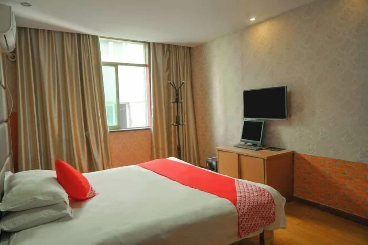 A hotel room with a bed, a television, a desk, and a window with curtains.