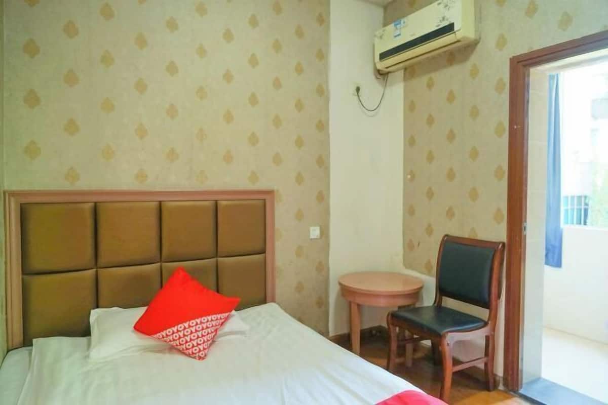 A hotel room with a bed, a chair, a small table, and an air conditioning unit.