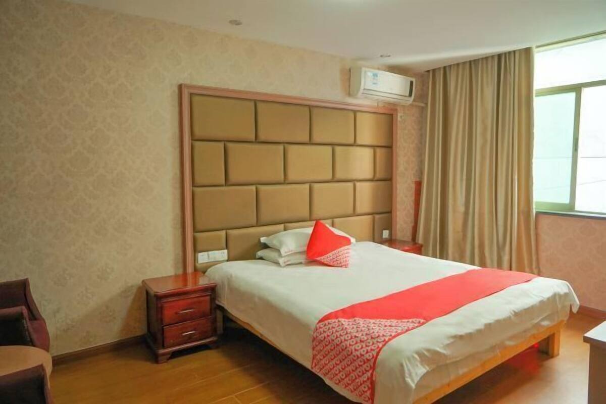 A hotel room with a large bed, a nightstand, a chair, and a window with curtains.
