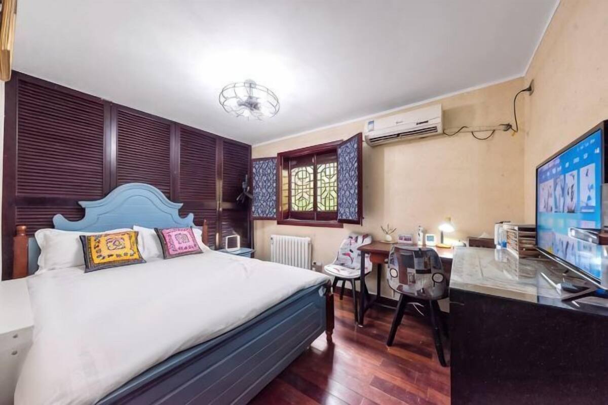 Une chambre à coucher comprenant un lit, un bureau, une chaise, un téléviseur et une fenêtre avec des volets à motifs.