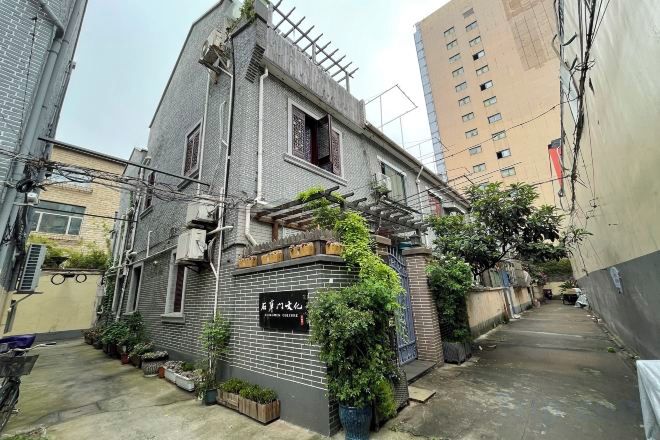 Un estrecho callejón con un edificio a la izquierda, un pequeño jardín con plantas y un edificio alto al fondo.