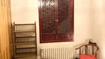 A room with a glass table, a wooden chair with a red cushion, a wooden shelf, and a window with a decorative wooden frame.