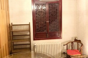 A room with a glass table, a wooden chair with a red cushion, a wooden shelf, and a window with a decorative wooden frame. - Shanghai Shikumen Culture Homestay (Shanghai)