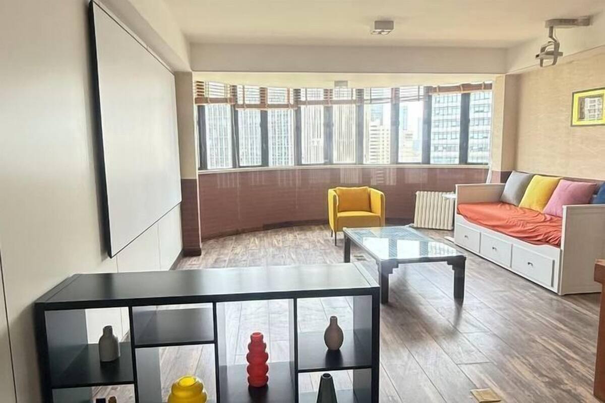 Un salon moderne avec un canapé, un fauteuil jaune, une table basse en verre et une table d’appoint noire agrémentée d’objets décoratifs.