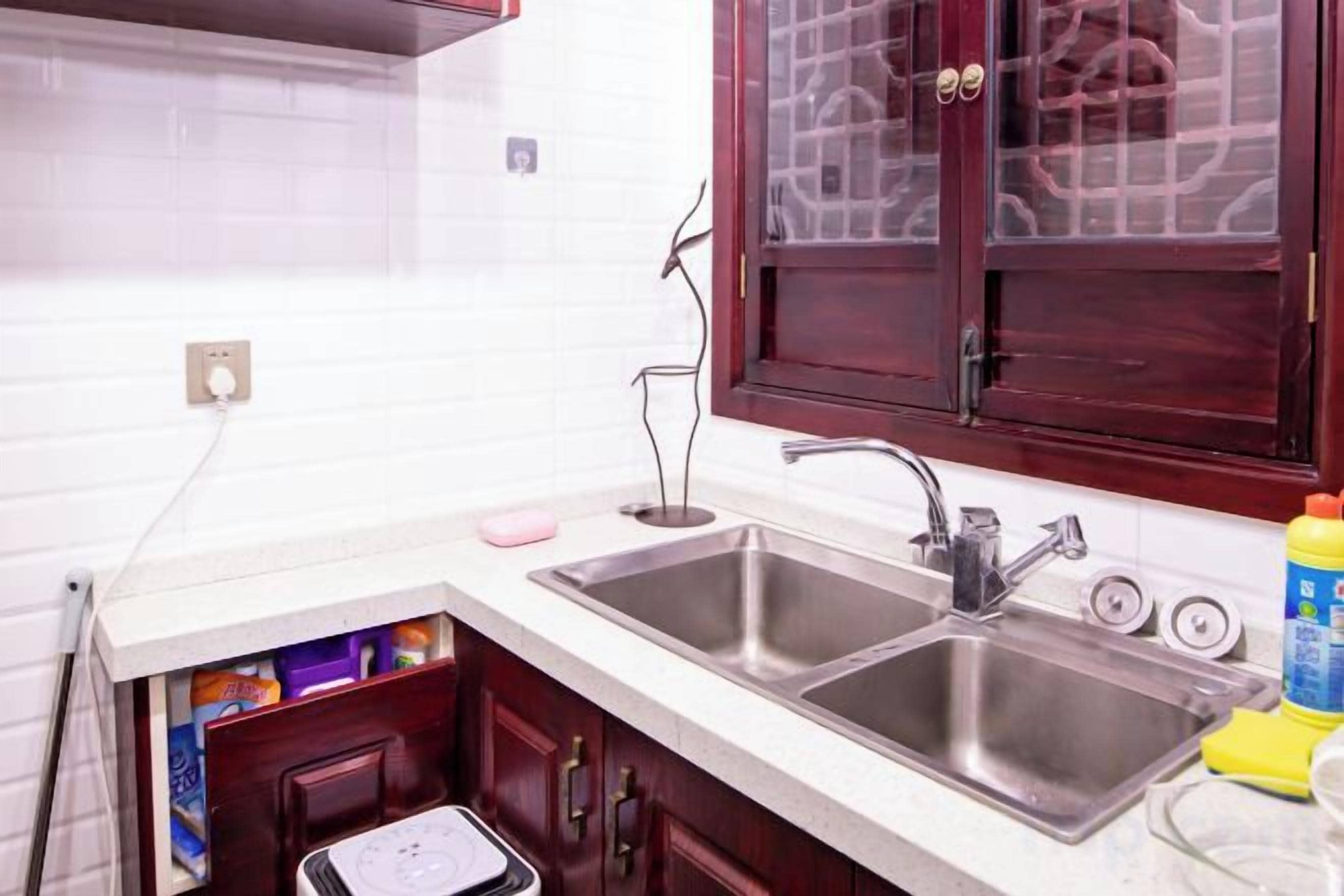 A kitchen with two stainless steel sinks, a white countertop, and a wooden cabinet with a window above.
