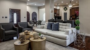 Un salon spacieux avec un canapé beige, des fauteuils foncés et un coin repas agrémenté d’un lustre.