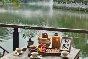 Una mesa con comida y bebidas, una planta en maceta y un cartel con caracteres chinos, con vista a un lago.