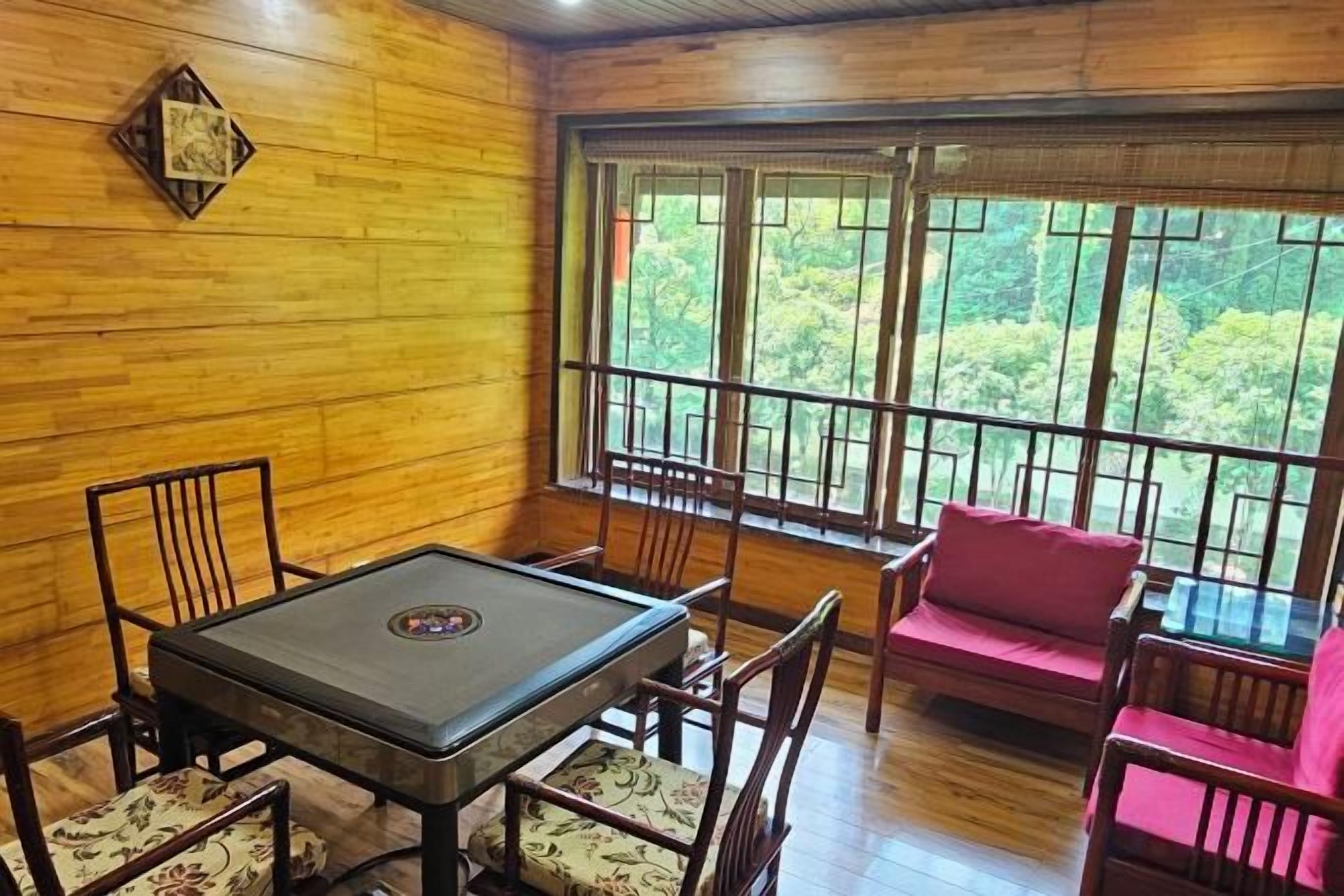 A room with a wooden interior, a table with chairs, a red sofa, and large windows with a view of greenery.