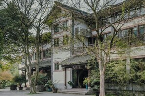 Un edificio tradicional con un porche cubierto, rodeado de árboles y un cuerpo de agua.