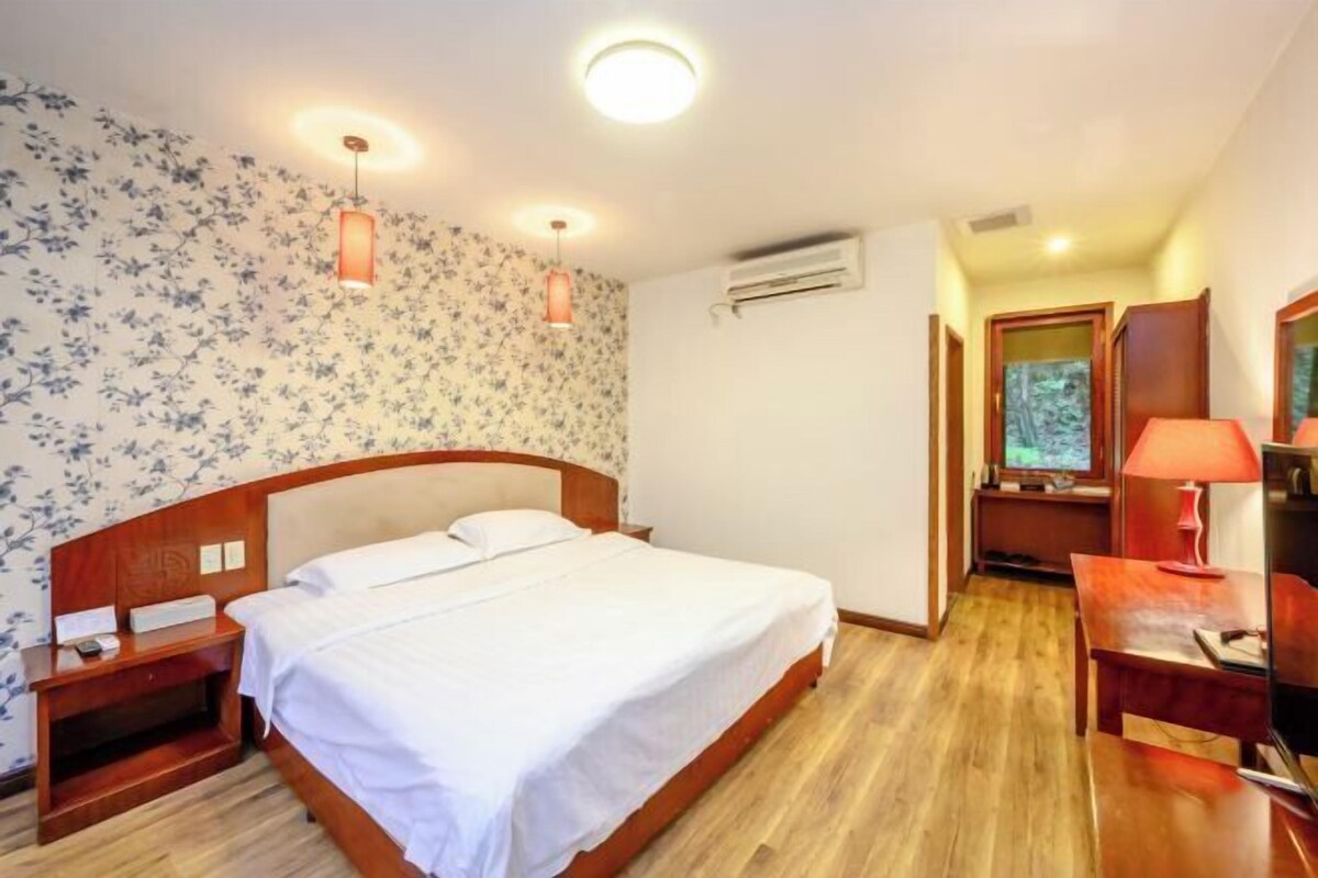 Una habitación de hotel con una cama de madera, una mesita de noche, un escritorio con lámpara y un televisor pequeño.