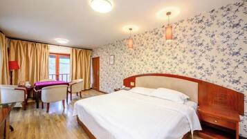 A hotel room with a large bed, a desk with a chair, a small table, and a window with curtains.