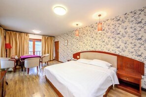 Habitación de hotel con una cama grande, un escritorio con silla, una mesita y una ventana con cortinas.