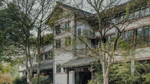 Um edifício tradicional de vários andares com um pátio, rodeado por árvores e plantas em vasos.