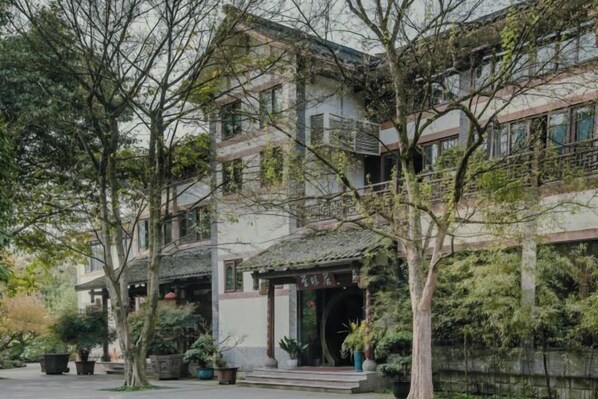 A traditional multi-story building with a courtyard, surrounded by trees and potted plants.