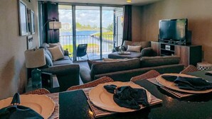 Una habitación de hotel amplia con balcón, un conjunto de sofás, televisión y un comedor con platos y cubiertos.