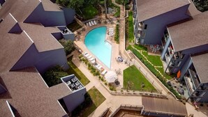 Vista aérea de un edificio residencial con piscina, rodeado de sillas de descanso y un césped cuidado.