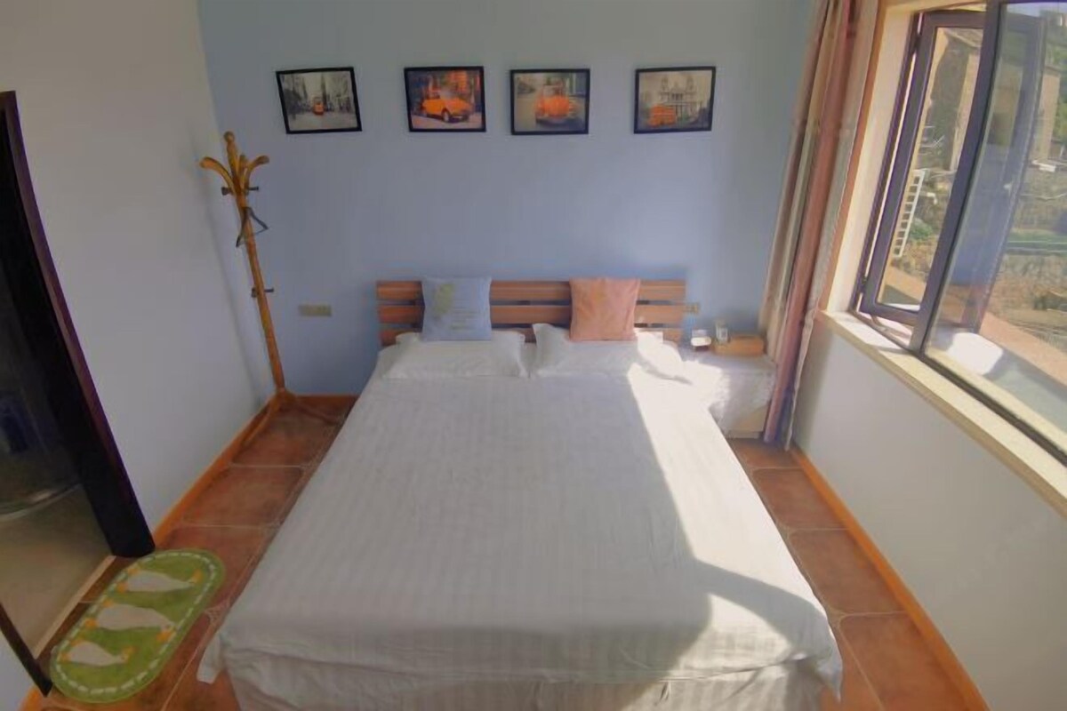 Un dormitorio con cama, cabecera de madera, ventana con vistas y cuadros en la pared.