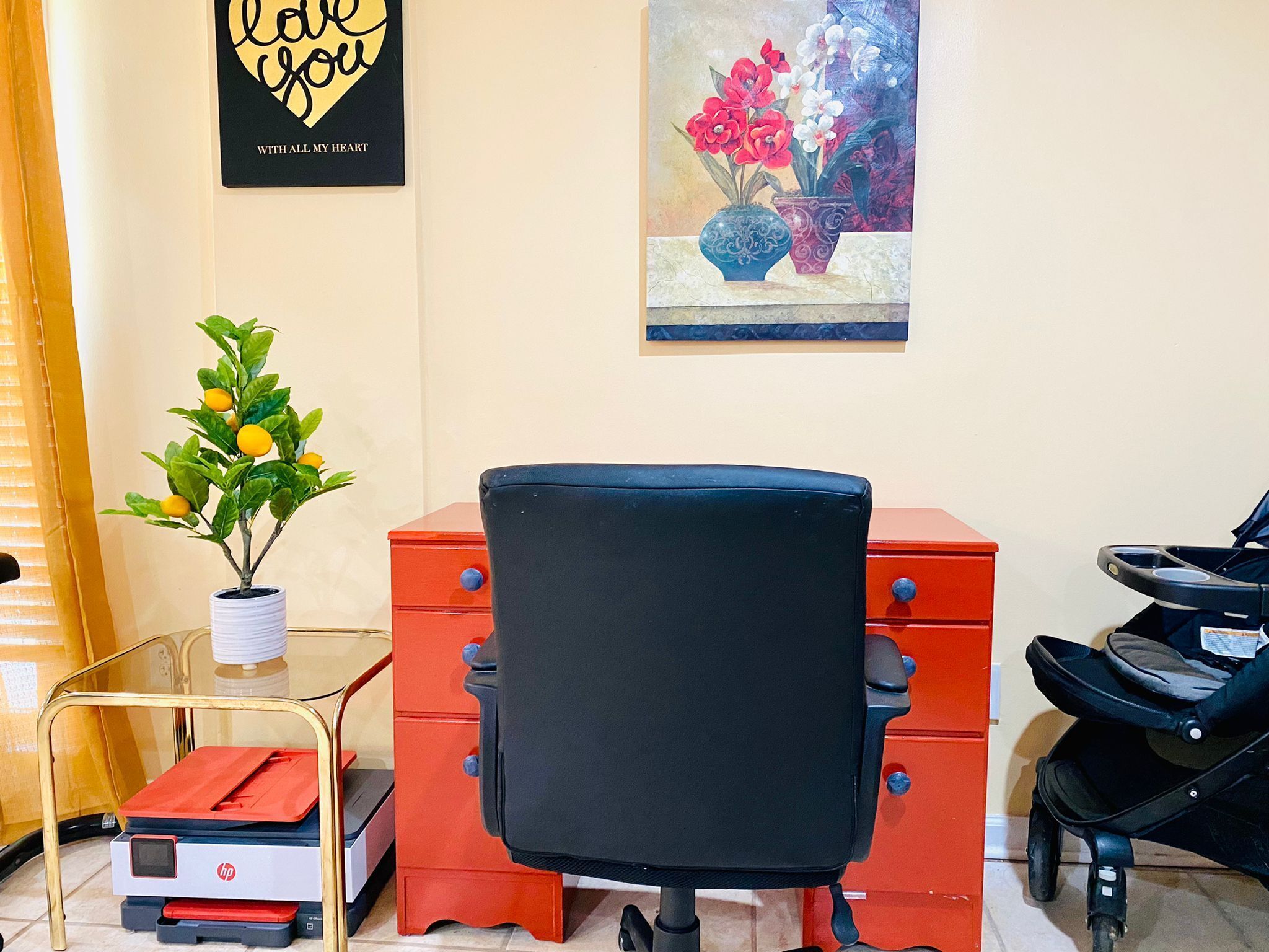 A room with a black office chair, a red filing cabinet, a small table with a potted plant, and a stroller.