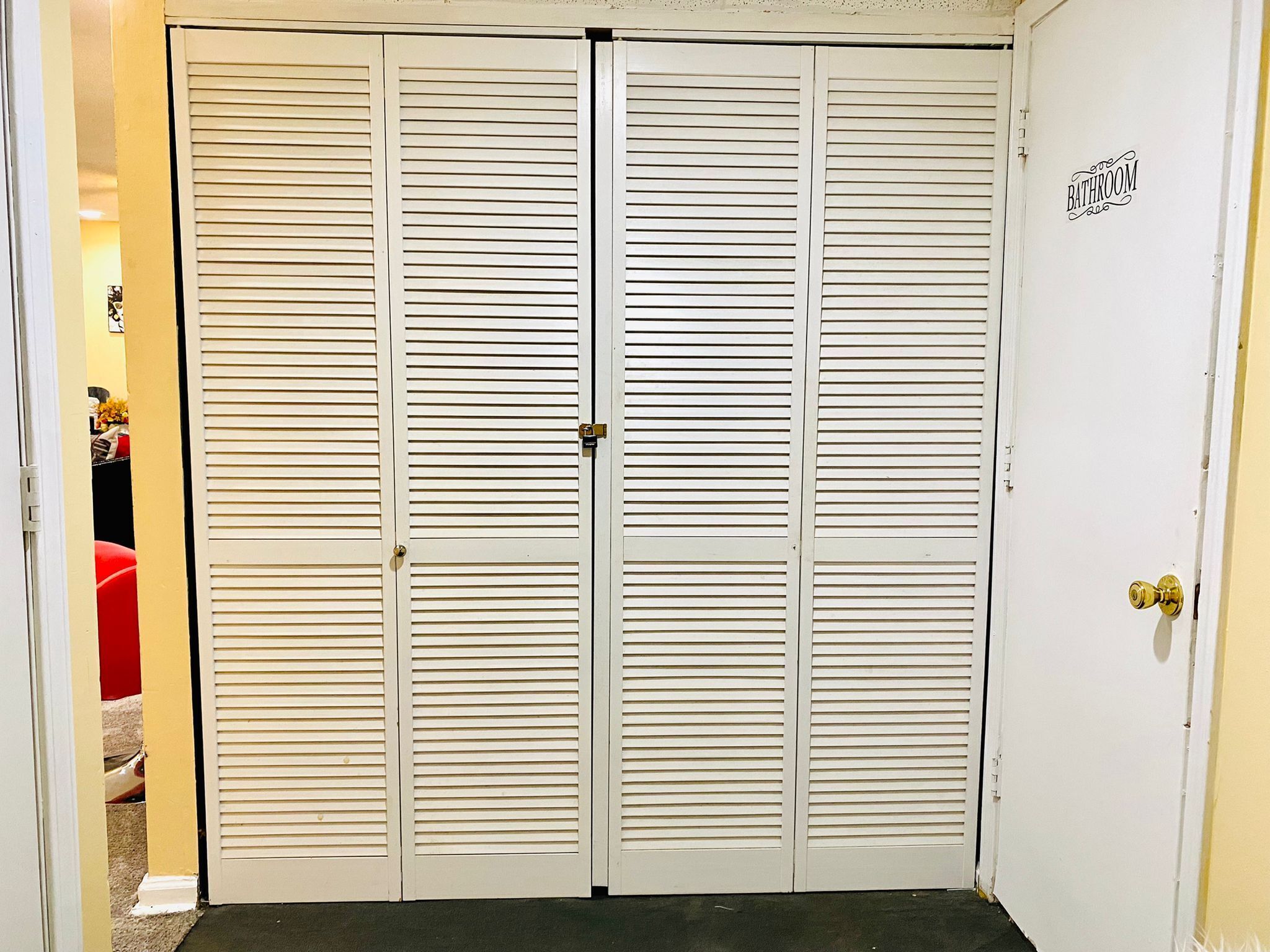 Un placard blanc fermé, doté de portes à persiennes horizontales, d’une poignée de porte en laiton et d’une pancarte indiquant « Salle de bain » sur le côté droit.