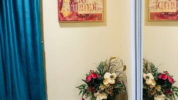A room with a teal curtain, a painting of Paris, and two flower arrangements.