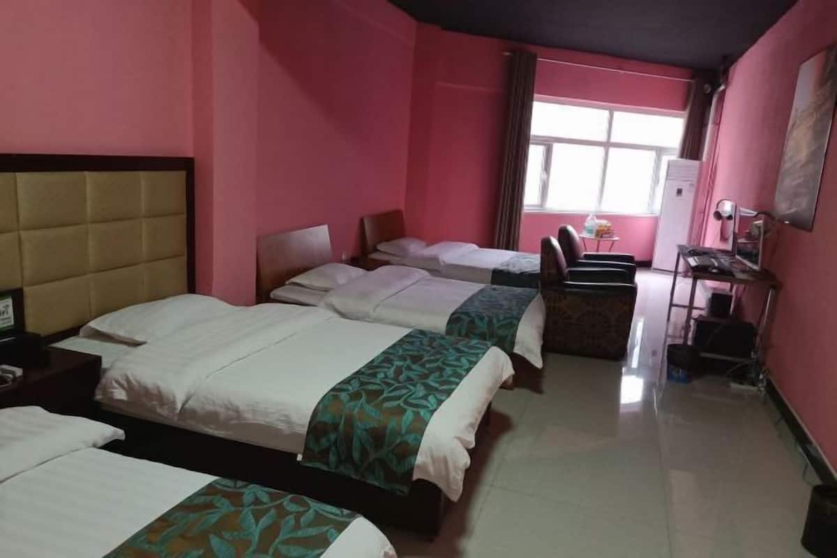 A hotel room with three beds, a desk, a chair, and a window.