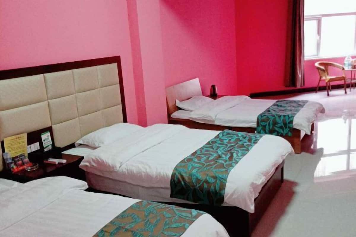 A hotel room with three beds, a wooden headboard, a small table, and a chair.