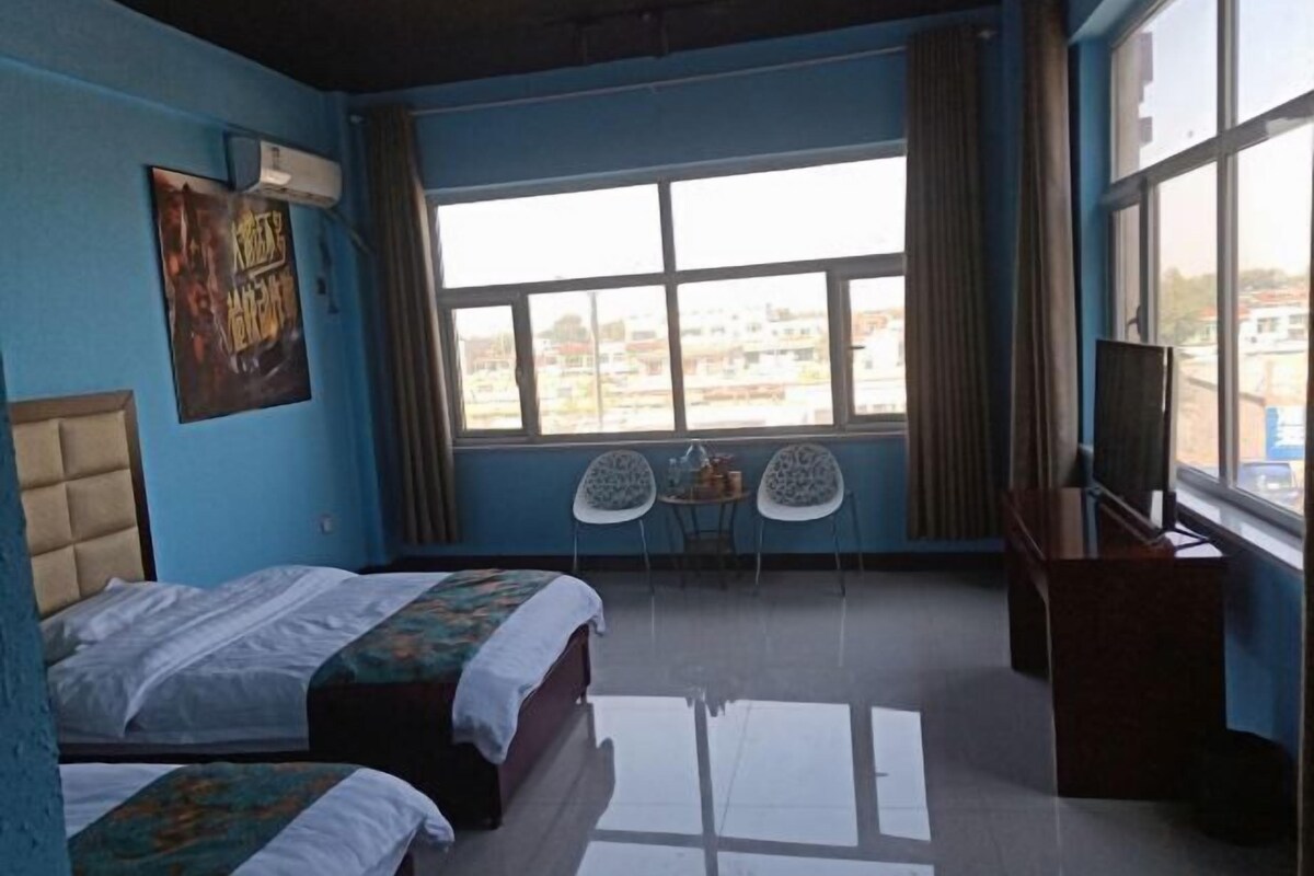 Ein Hotelzimmer mit zwei Betten, einem Schreibtisch, einem Sessel, einem Fernseher und einem großen Fenster mit Blick auf die Stadt.