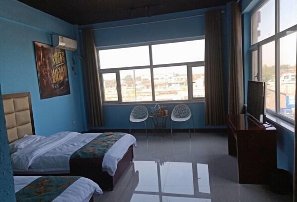 Ein Hotelzimmer mit zwei Betten, einem Schreibtisch, einem Sessel, einem Fernseher und einem großen Fenster mit Blick auf die Stadt.