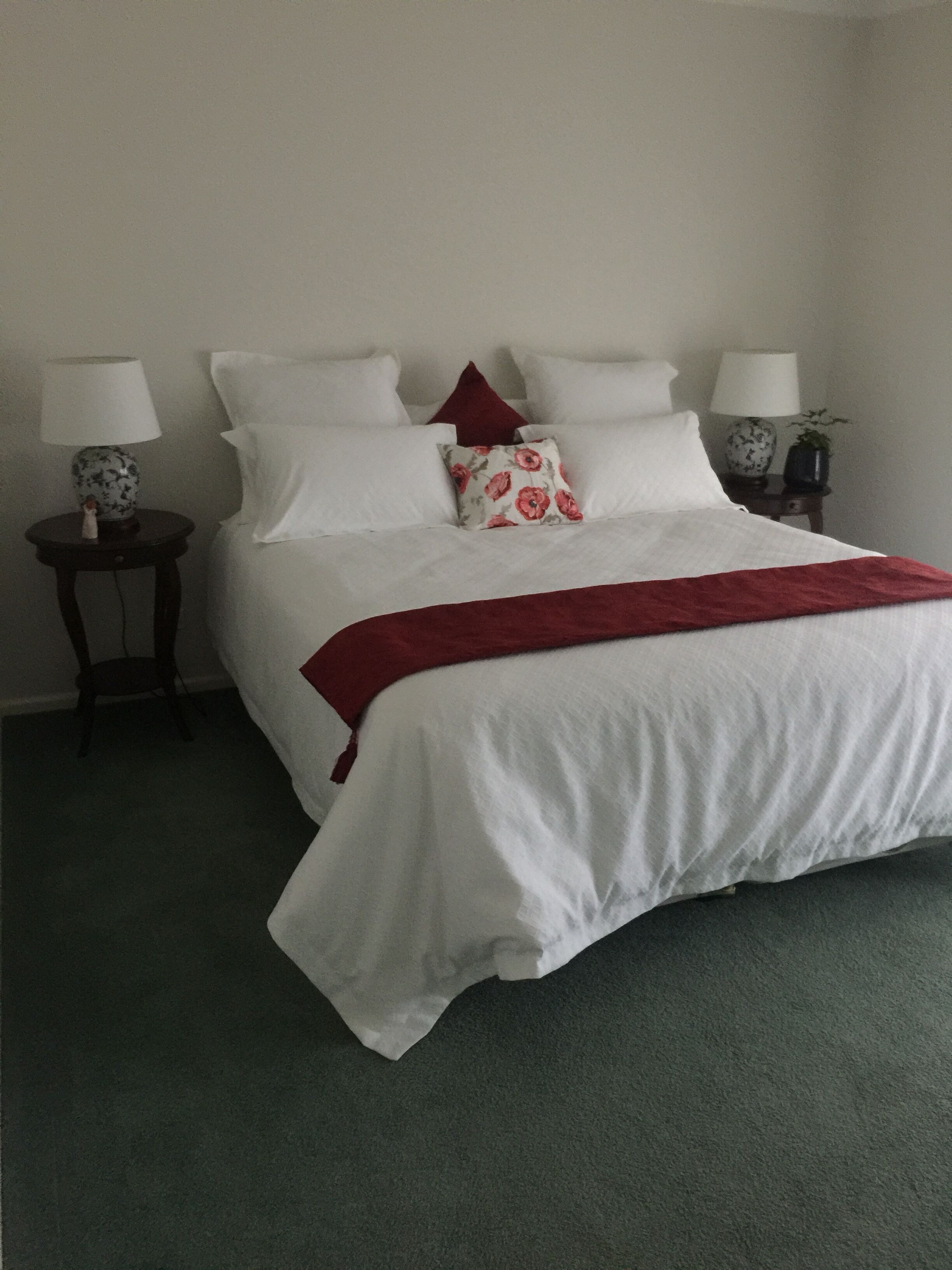 Ein ordentlich bezogenes Bett mit weißer Bettwäsche und einer roten Decke, zwei Nachttische mit Lampen sowie eine kleine Pflanze auf einem Tisch.