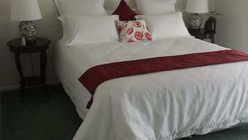 Un lit bien fait, avec une literie blanche et un plaid rouge, deux tables de chevet avec des lampes, et une petite plante posée sur l’une des tables.