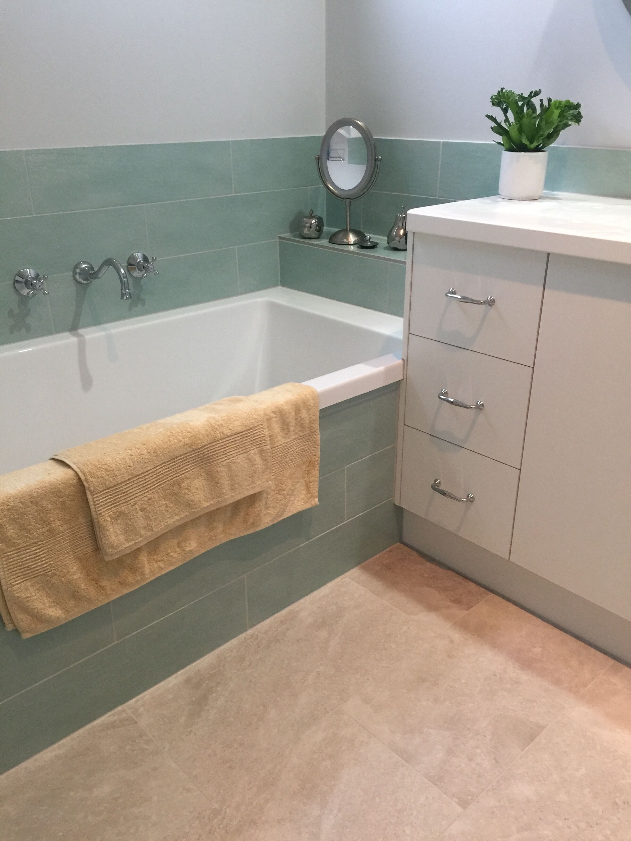 A bathroom with a bathtub, a sink, a mirror, and a potted plant.