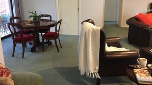 A living room with a dining table, chairs, a leather sofa, a coffee table, and a bookshelf. - Bird Abode Accommodation in central Maryborough (Maryborough)