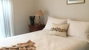 A neatly made bed with a beige blanket, a bedside table with a lamp, and a framed picture on the wall. - Bird Abode Accommodation in central Maryborough (Maryborough)